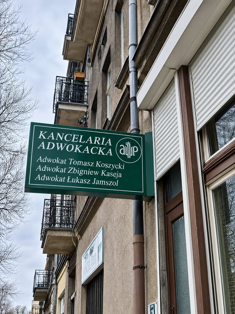 Zielony szyld Kancelarii Adwokackiej nad wejściem przy ul. Kazimierzowskiej 10 w Kaliszu, z nazwiskami adwokatów Koszyckiego, Kaseji i Jamszoła